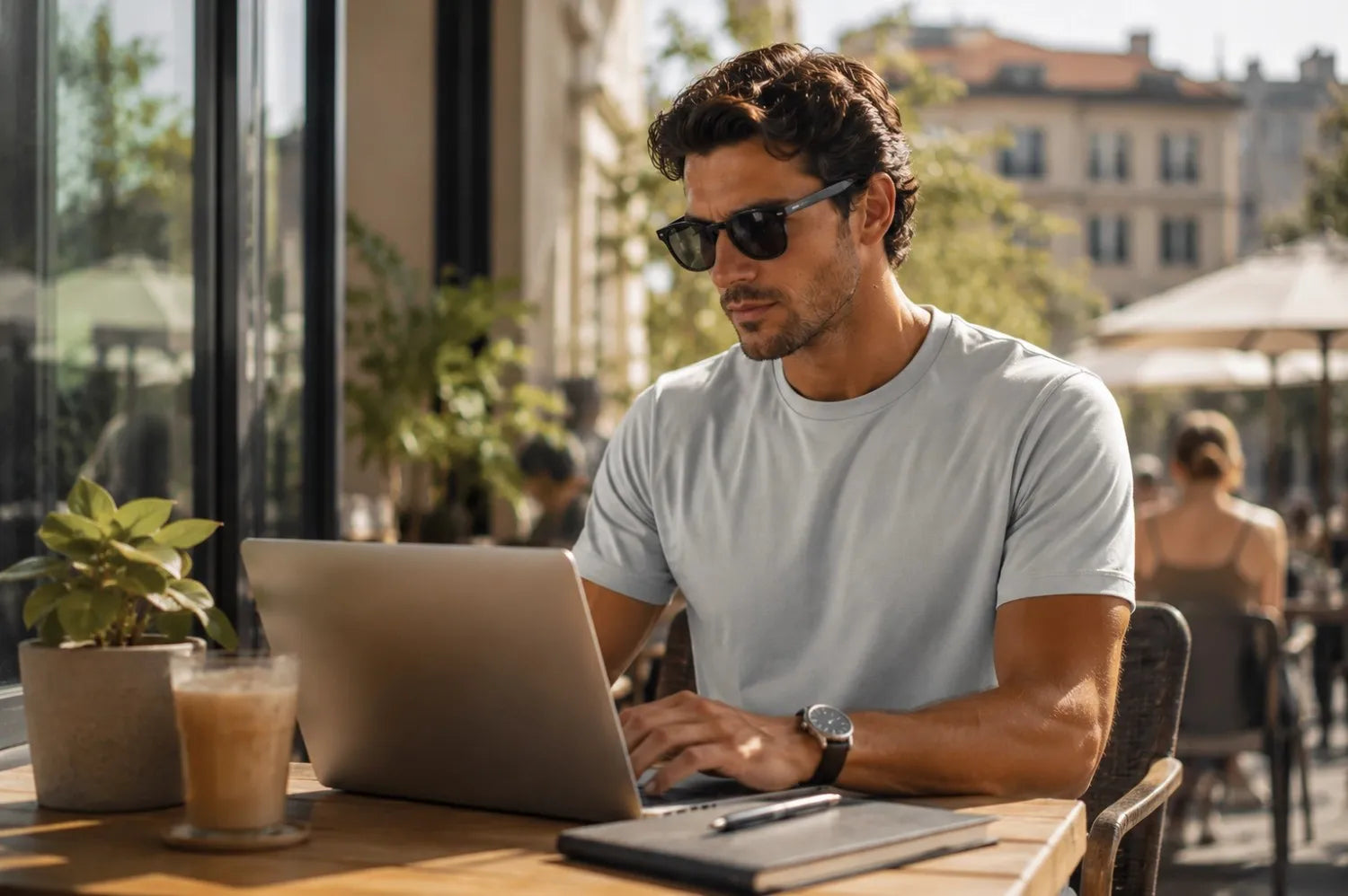 Man using a laptop at an outdoor cafe with a cityscape in the background