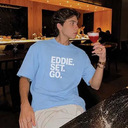 A man wearing a light blue crewneck t-shirt with the text 'EDDIE. SET.