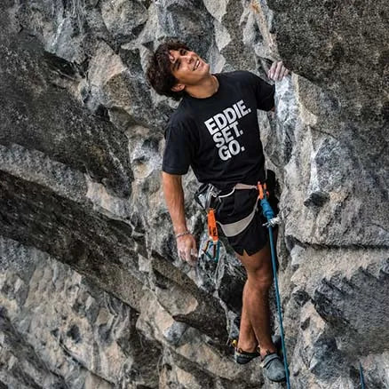 A male rock climber wearing a black graphic t-shirt with the text 'EDDIE. SET.