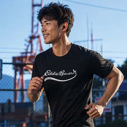 A man running outdoors wearing a black short-sleeve athletic T-shirt with a white 'Eddie Bauer' logo across the chest.