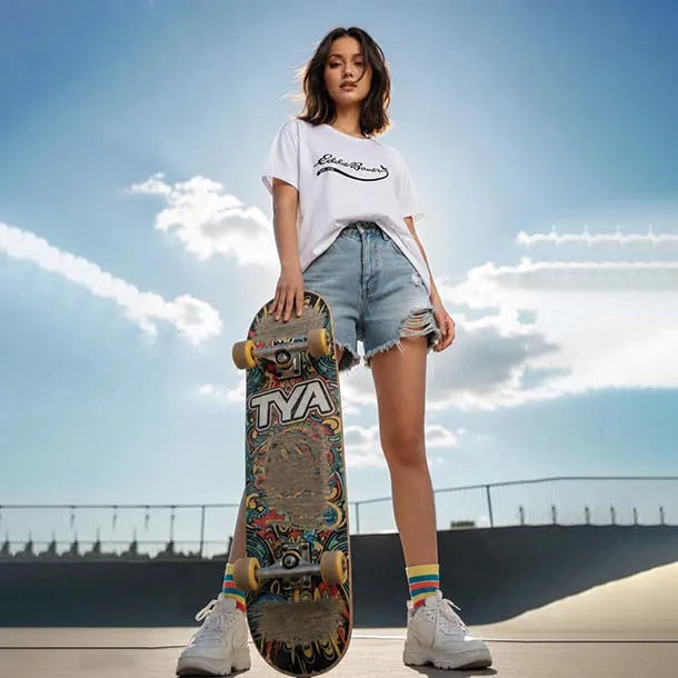 A young woman stands in a skatepark holding a colorful graphic skateboard, wearing a white graphic t-shirt, light-wash denim shorts, and white sneakers against a blue sky background.